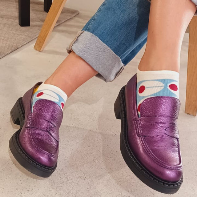Purple loafers worn with rolled-up jeans on a light-colored floor.