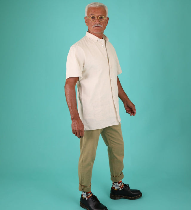 A standing man, dressed in a short-sleeved beige shirt and rolled-up khaki trousers. He shows off his geometric patterned socks, combined with black shoes.