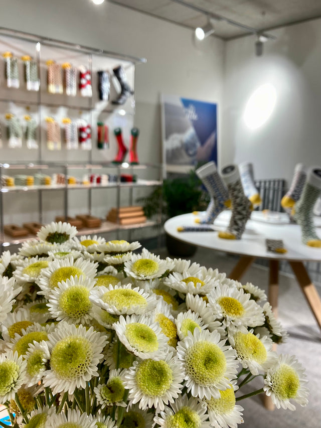 In this interior view of the SirTile store, a vibrant bouquet of flowers takes the foreground, while socks over a round table and hanging in a cupboard add a touch of colour to the background.