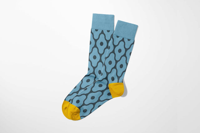 A digital mockup of a pair of blue socks adorned with geometric motifs, featuring a yellow toe cap and heel, on a light grey background.