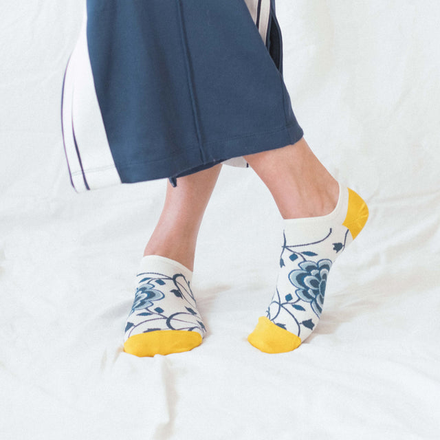 Person wearing blue pants and patterned ankle socks with yellow toes on a white background