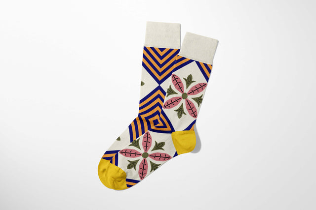A digital mockup featuring colourful socks combining purple and orange diamond shapes and pink flowers with green leaves, mustard toes and heels, set against a light grey background.