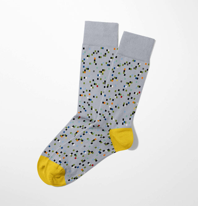 Pair of gray Miguel Bombarda socks featuring a colorful pixel pattern and yellow toes on a white background, ideal for injecting some fun into your minimalist wardrobe. Made from luxurious Egyptian cotton, these socks provide both style and comfort.