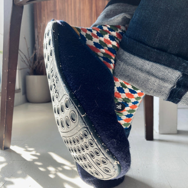 A foot is crossed over the other, adorned with Camper Wabi slippers and jeans, showcasing colorful geometric socks.