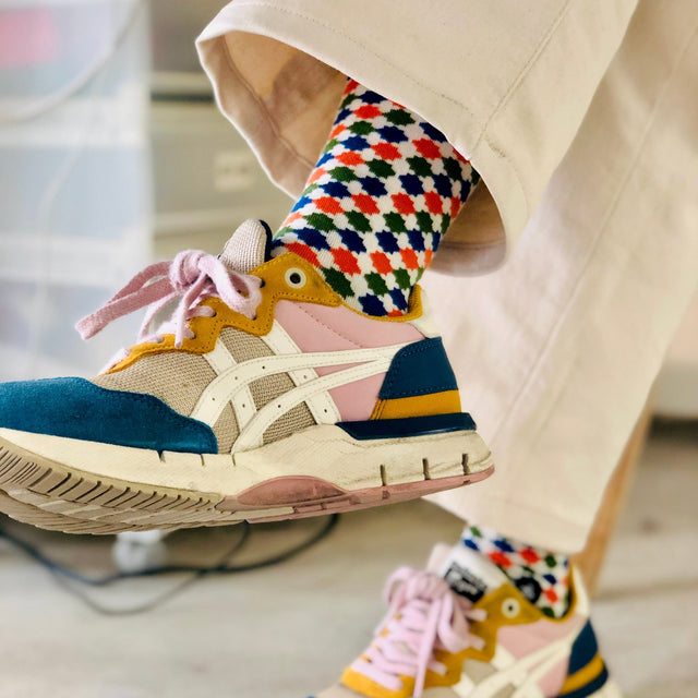 The crossed legs of a person clad in beige trousers reveal colorful geometric socks peeking out, paired with Onitsuka Tiger sneakers in blue and yellow.
